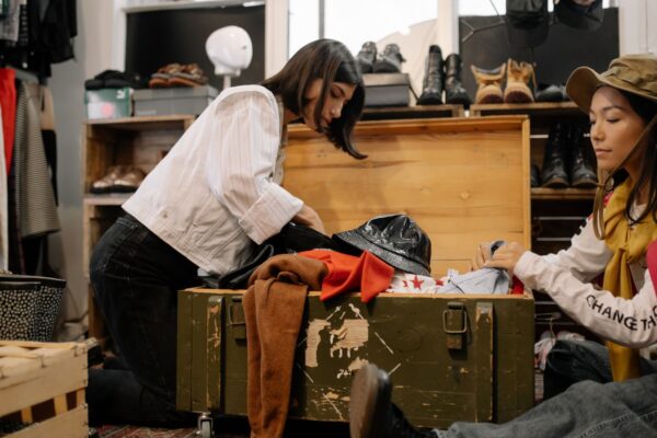 靴や帽子に囲まれた古着店で服を選ぶ二人の客（鹿児島の古着屋ガイドのイメージ）